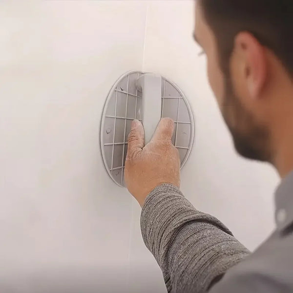 A person is holding a gray self-adhesive half circle sanding pad holder against a white wall.