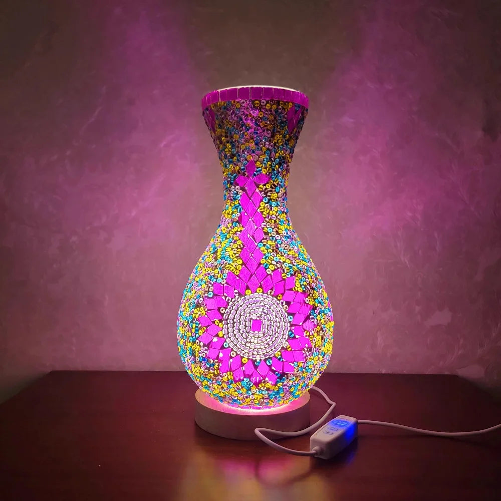 Lámpara de mesa de vidrio con incrustaciones a mano y diseño de mosaico multicolor iluminada contra un fondo púrpura.