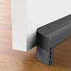 A gray door draft stopper with a slotted opening rests on a wooden surface next to a white cabinet.