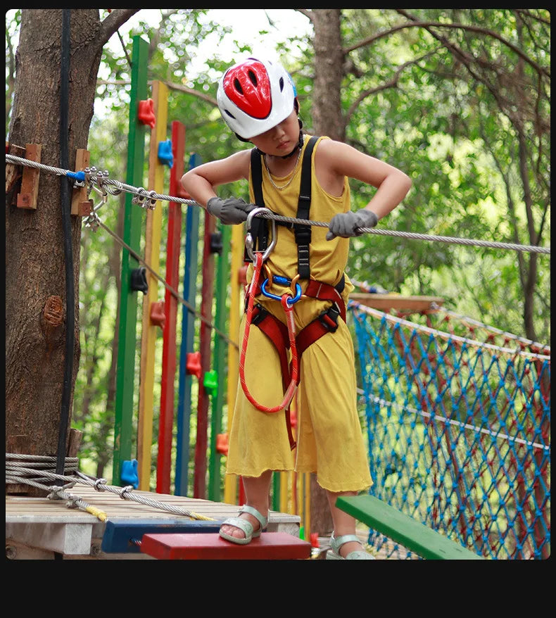 Un enfant portant un casque rouge participe à une activité d'escalade en extérieur avec une corde à boucle.