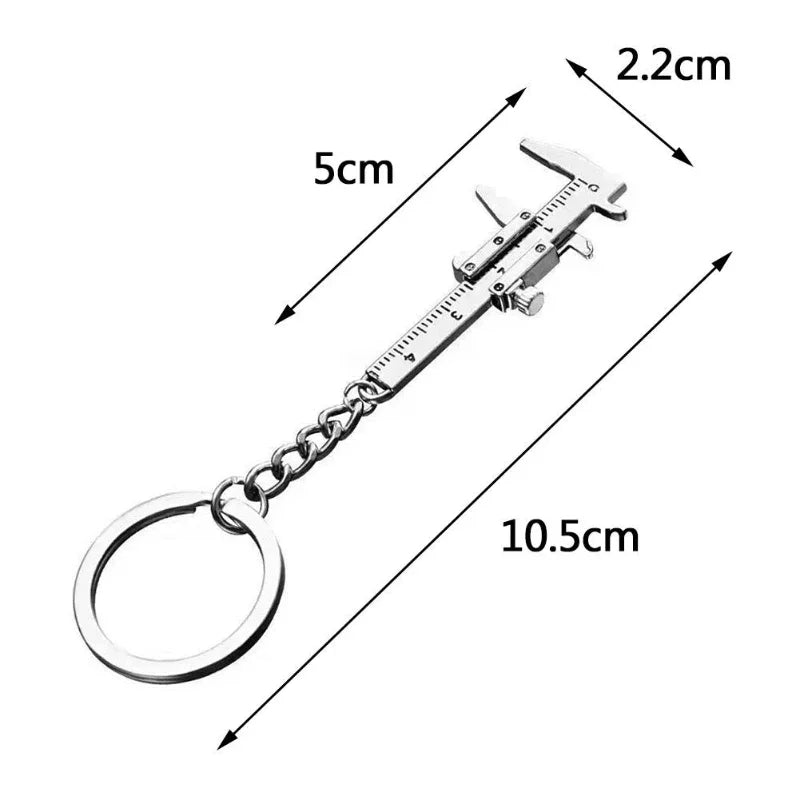A silver metal jewelry measuring ruler and caliper keychain with a loop and a small tool visible.