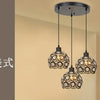 A modern chandelier lamp with multiple crystal globes hangs from a dark ceiling mount in a light-colored room.