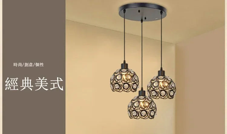 A modern chandelier lamp with multiple crystal globes hangs from a dark ceiling mount in a light-colored room.