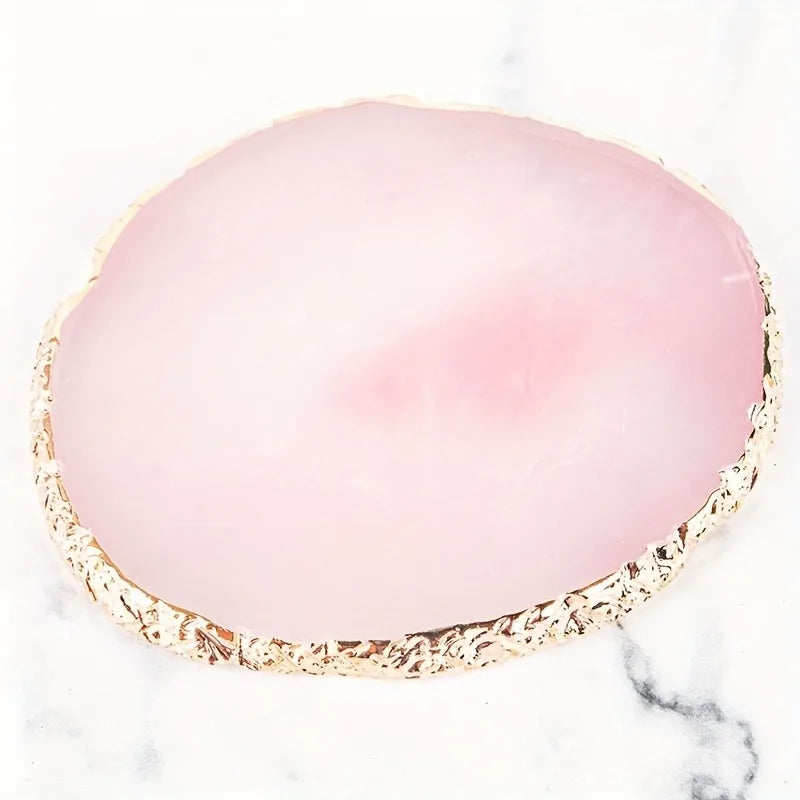 A round, translucent pink nail art brush set with a textured gold rim on a white marble surface.