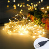 Un faisceau de guirlandes lumineuses en fil de cuivre blanc chaud avec de petites ampoules LED sur une surface sombre.