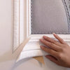 A hand is pressing a white 3D embossed flexible foam wall trim molding against a gray textured panel.