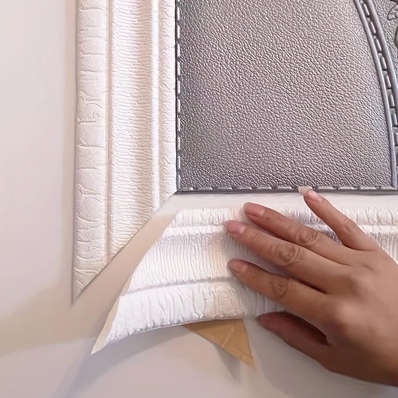 A hand is pressing a white 3D embossed flexible foam wall trim molding against a gray textured panel.