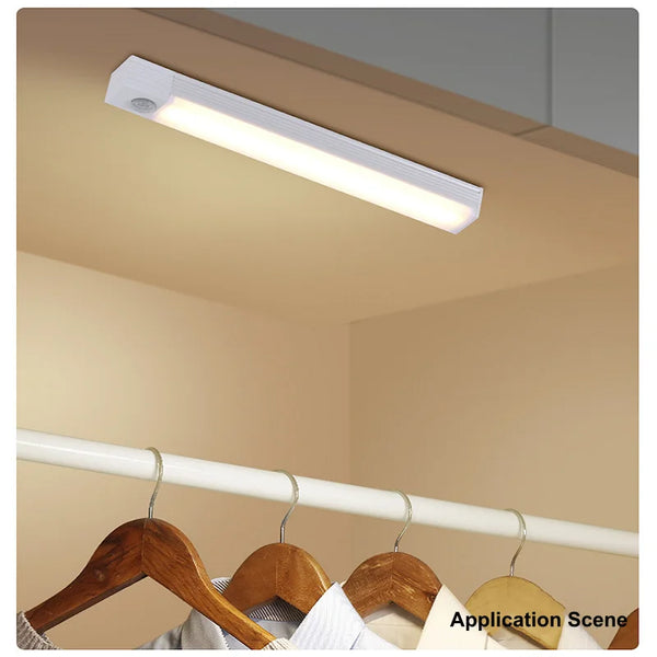 A long, rectangular LED light bar is mounted on a ceiling, illuminating a room. The light is white and emits a bright glow.