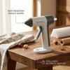A white cordless hot glue gun with a heat-resistant nozzle guard sits on a wooden table.