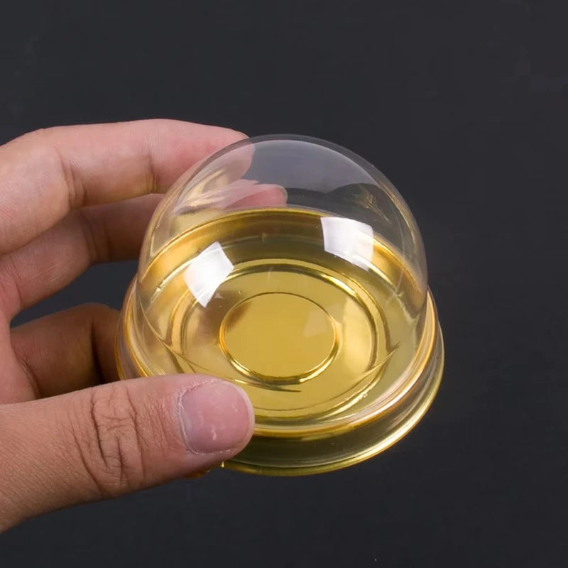 Eine Hand hält eine durchsichtige Plastik-Mini-Cupcake- und Muffinfach, gefüllt mit goldfarliquide.