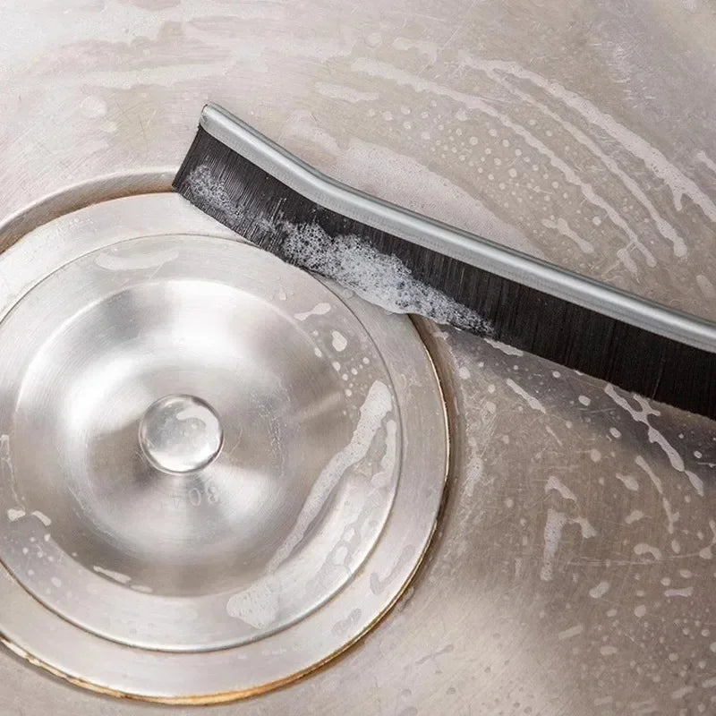 A close-up of a metal grout gap cleaning brush with a silver head resting on a stainless steel surface.