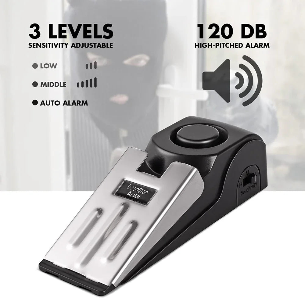 A black portable door stopper alarm device with a silver plate, shown against a blurred background.