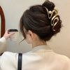 A woman with dark hair styled in an updo is shown from the back, wearing elegant gold S-shaped metal hair clips.