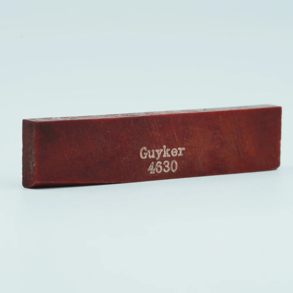 A wooden acoustic guitar bone bridge saddle with the inscription Guyker 4630