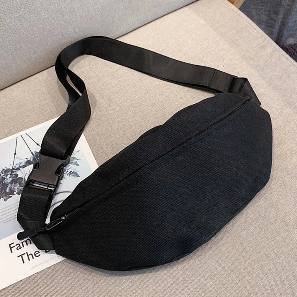 Black linen crossbody waist bag with a black strap resting on a light beige surface.