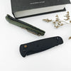 A folding utility knife in olive green is shown next to a black knife and a box.