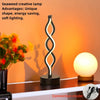 A black and white wavy seaweed creative desk lamp illuminating a round light bulb on a wooden surface.