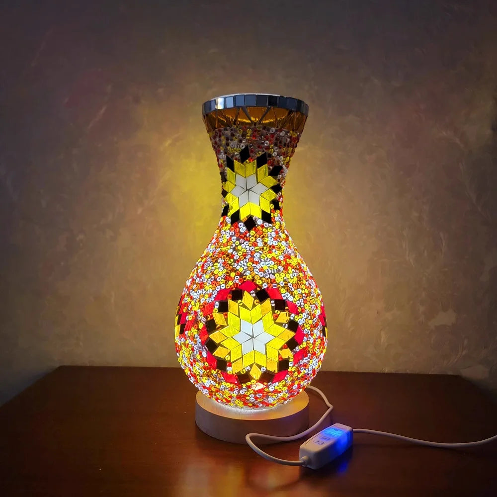 Lámpara de mesa de vidrio decorativa con diseño de mosaico multicolor sobre una superficie de madera.