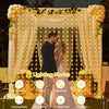 A couple is featured in a softly lit backdrop decorated with sheer curtains and string lights for an outdoor event.