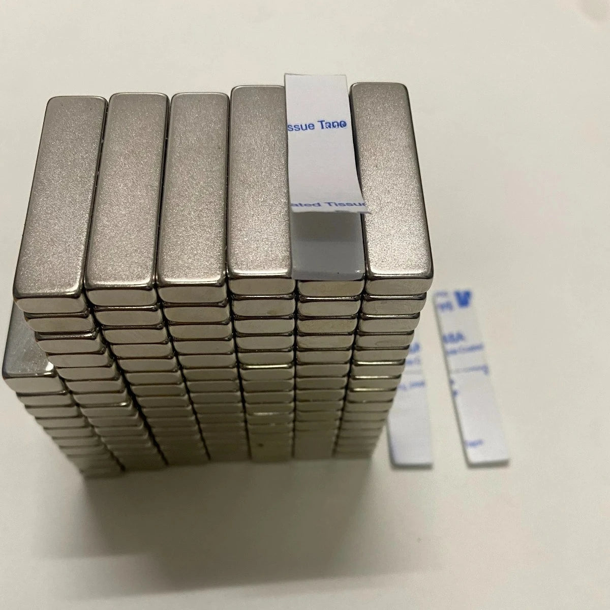 Une pile de bandes magnétiques en néodyme argentées avec des étiquettes blanches sur une surface blanche.