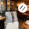 Un oreiller gris avec des sangles colorées est posé sur une valise blanche dans un café.