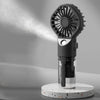 A black portable USB rechargeable mist fan with a circular grille is displayed on a white speckled base.