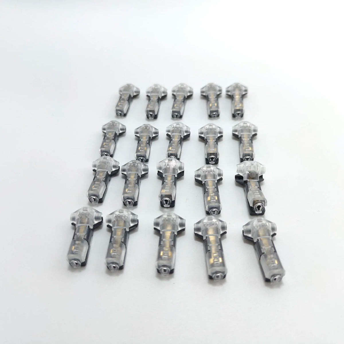 A collection of thirty T-type wire splice connectors in silver metal are arranged in a row on a white background.