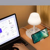 A laptop is open on a desk next to a white desk lamp that also functions as a charging socket.