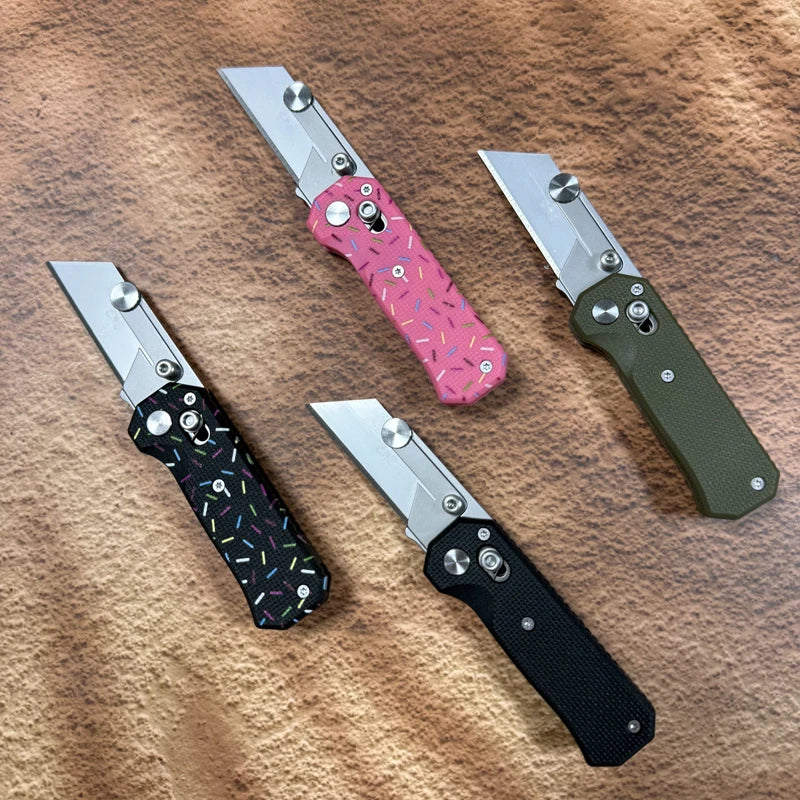 A collection of four folding utility knives with stainless steel blades and various colored handles resting on a brown fabric