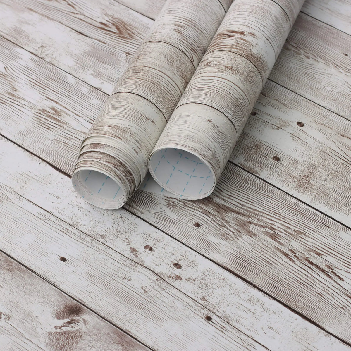 Rolls of retro wood grain self-adhesive wall stickers lying on a weathered white wooden surface.