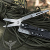A silver compact multi-tool pocket knife set is shown lying on a dark green cord.