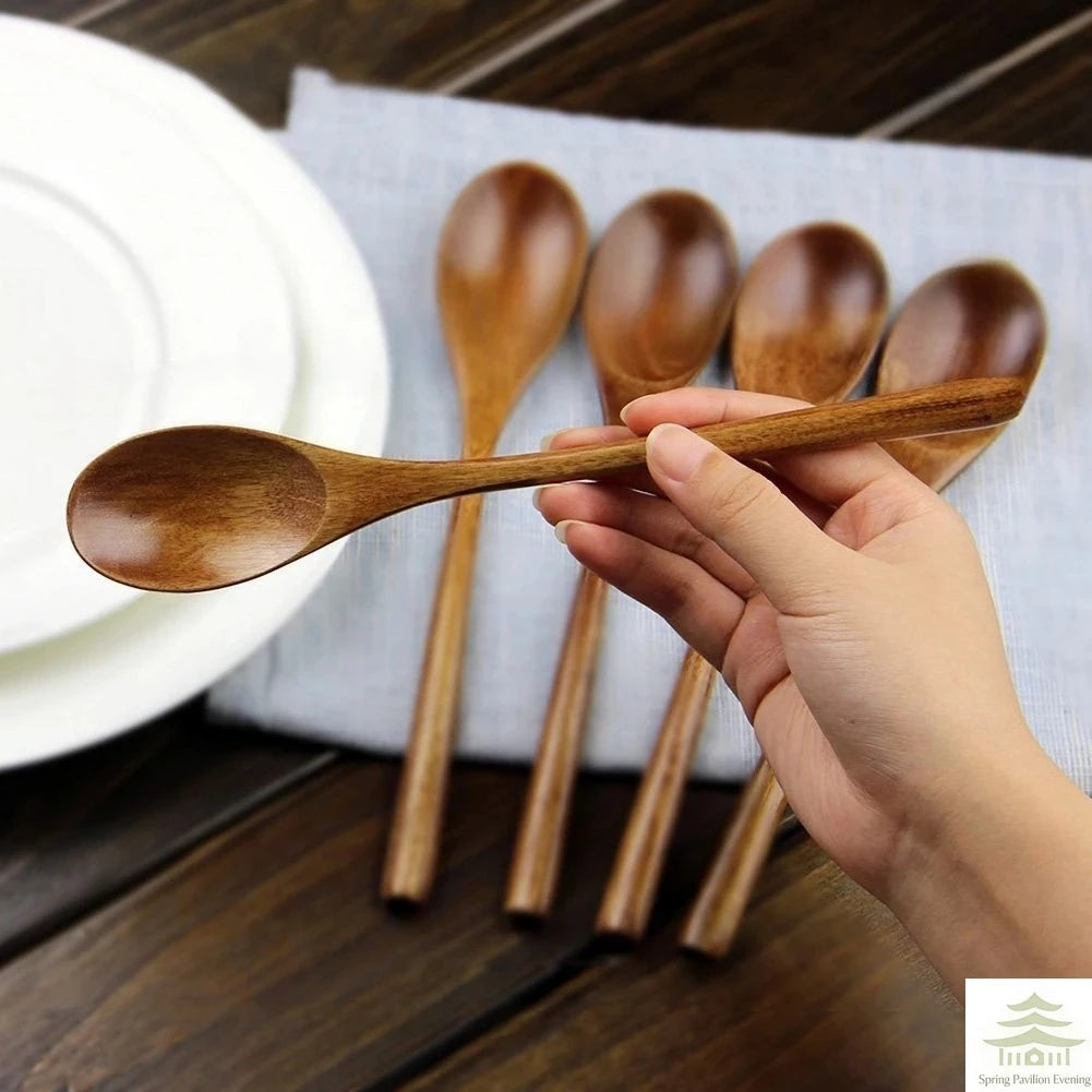 A hand holds a set of natural wooden spoons and forks resting on a white napkin next to a stack of plates.