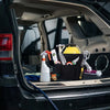 A black storage organizer basket filled with various tools and cleaning supplies is placed on the interior of a car door pane