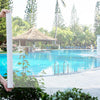 Eine Hand hält ein weißes, wiederverwendbares, selbstklebendes Moskitonetz in der Nähe eines leuchtend blauen Swimmingpools u