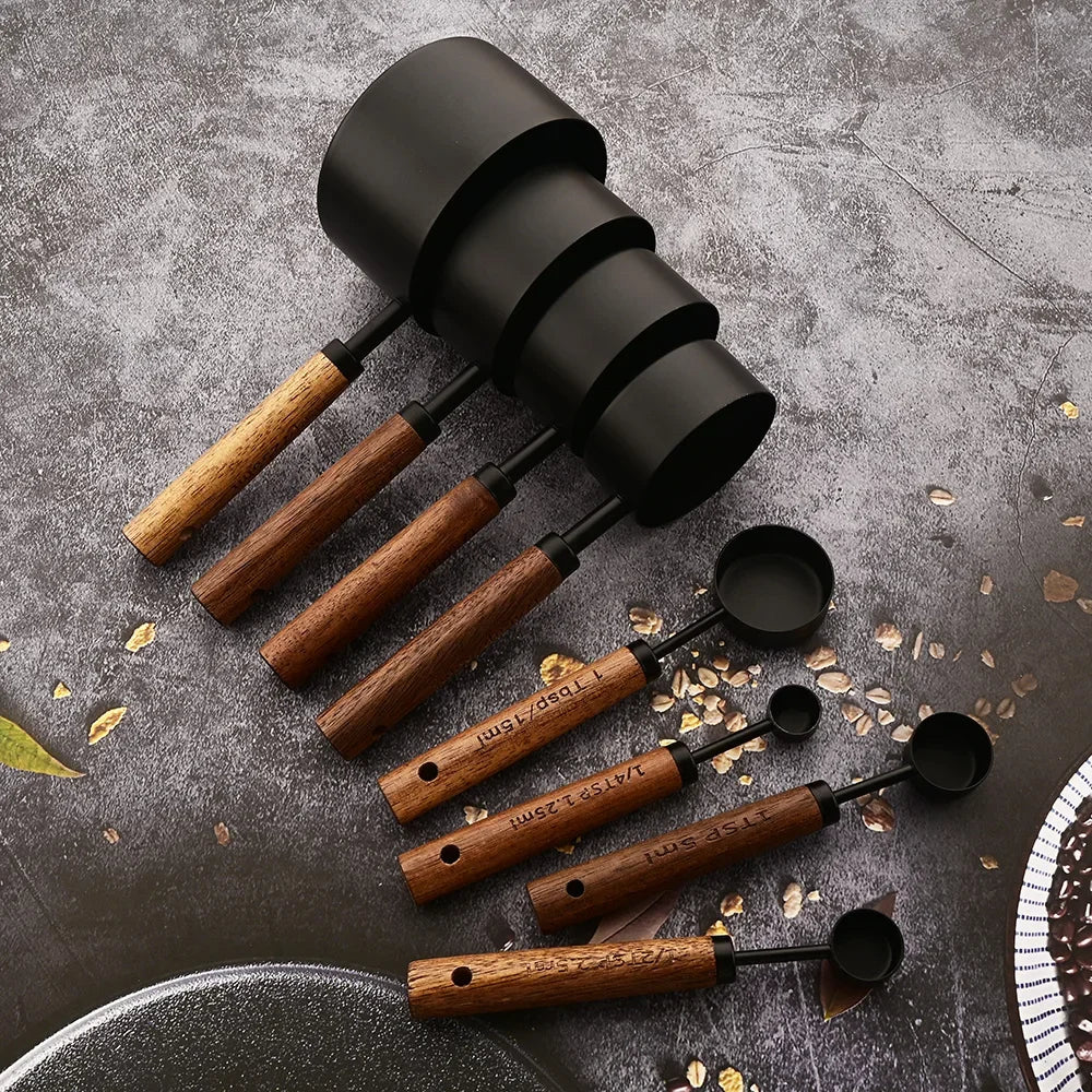 A set of stainless steel and wooden measuring spoons arranged on a dark gray surface.