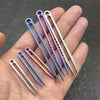 A hand holds several titanium clip tweezers with gradient purple and pink coloring.