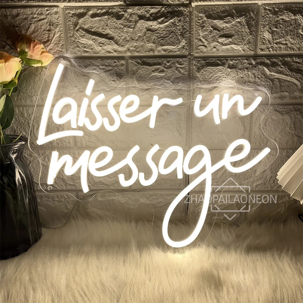 A white neon sign spelling out 'Laisser un message' is displayed on a textured gray brick wall with a fluffy white rug.