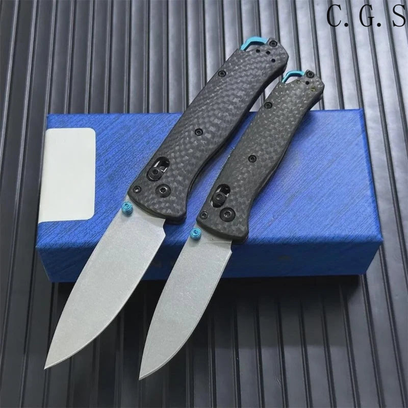 A pair of carbon fiber folding knives are displayed on a blue box against a dark background.