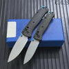 A pair of carbon fiber folding knives are displayed on a blue box against a dark background.