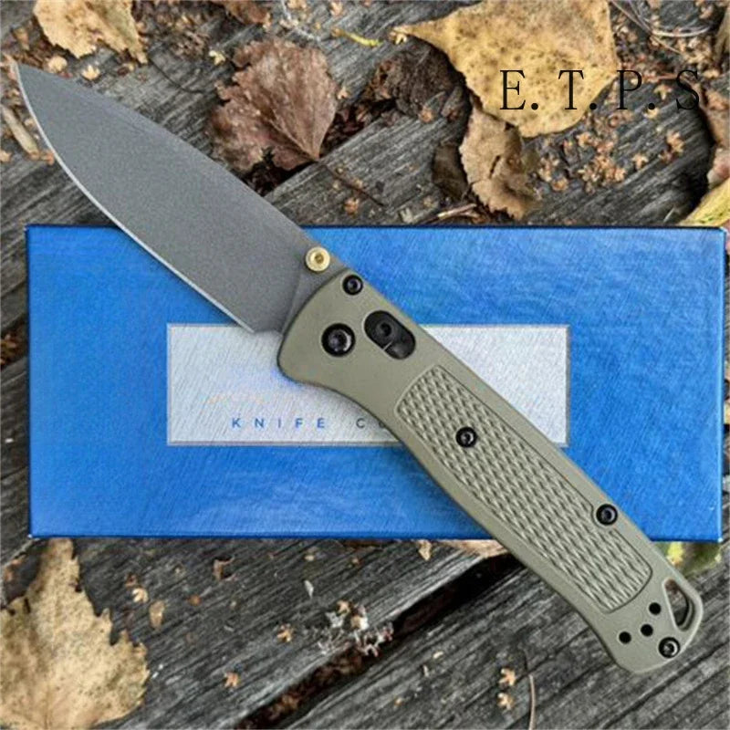 A folding EDC pocket knife with a gray blade and a tan handle rests on a blue surface amidst dry leaves.