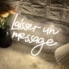 A glowing white neon sign shaped like the words 'Laisser un message' is displayed on a textured wall above a fluffy white rug