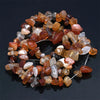 A collection of natural, tumbled agate beads in various shades of amber, brown, and pink are displayed on a dark surface.