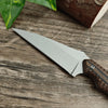 A silver compact fixed blade utility knife rests on a wooden surface next to a green leaf and a piece of wood.