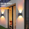 Una luz de pared solar iluminando una pared exterior blanca junto a una puerta de vidrio.