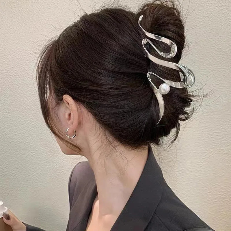 A close-up of a woman's dark hair styled in an elegant updo with gold S-shaped metal hair clips.