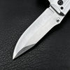 A silver premium folding utility pocket knife blade resting on a black leather surface.