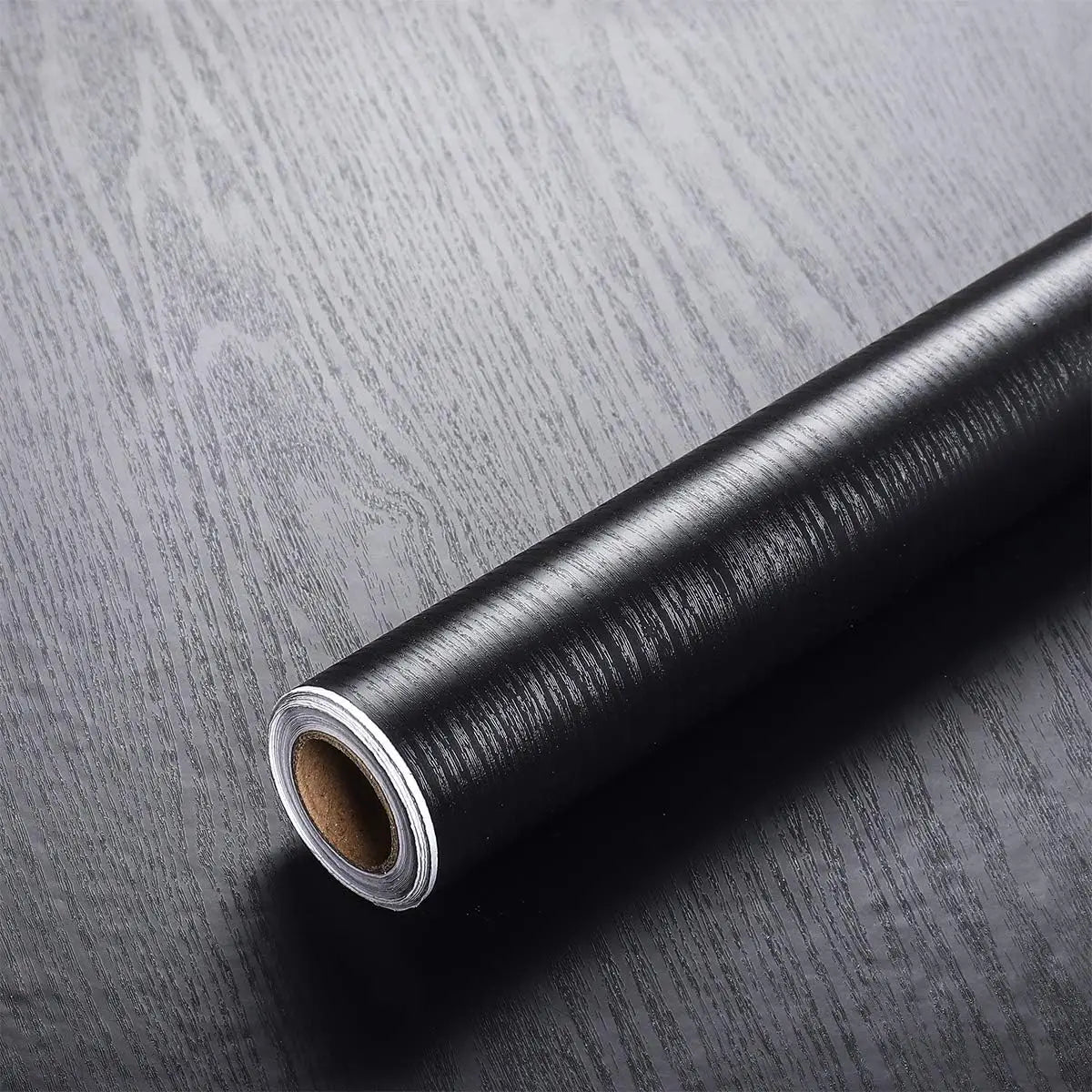 Roll of black wood grain vinyl wall contact paper lying on a dark surface