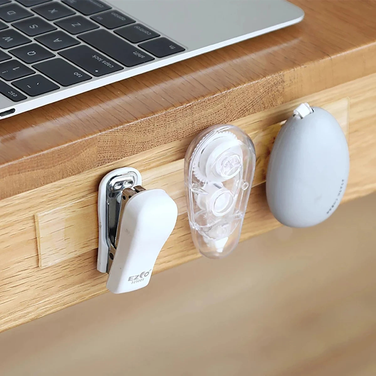 A white mounting tape dispenser with a clear roll is mounted on a wooden desk next to a white spherical object.