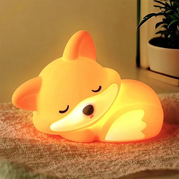 A glowing orange fox night light shaped like a sleeping animal resting on a textured surface.