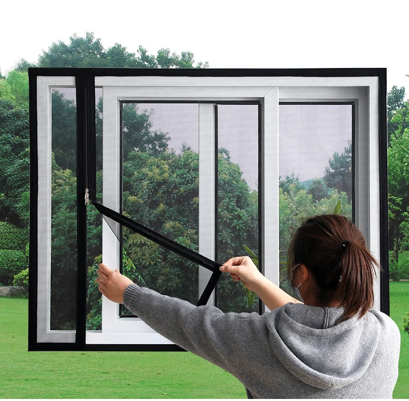 A person is installing a custom sized window mesh screen with a self-adhesive zipper into a white window frame.